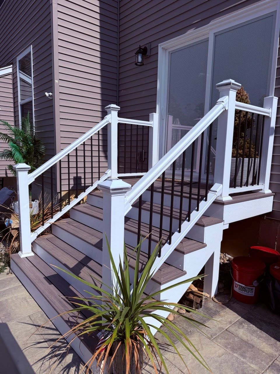 Wooden deck stairs with white railing and black spindles leading to a sliding glass door.