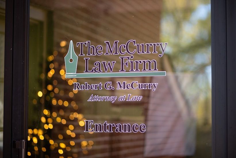 The McCurry Law Firm sign on a glass door, with a blurred holiday light background.