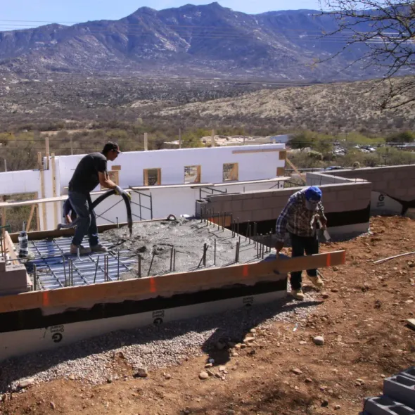 Two men are working on a construction site with mountains in the background