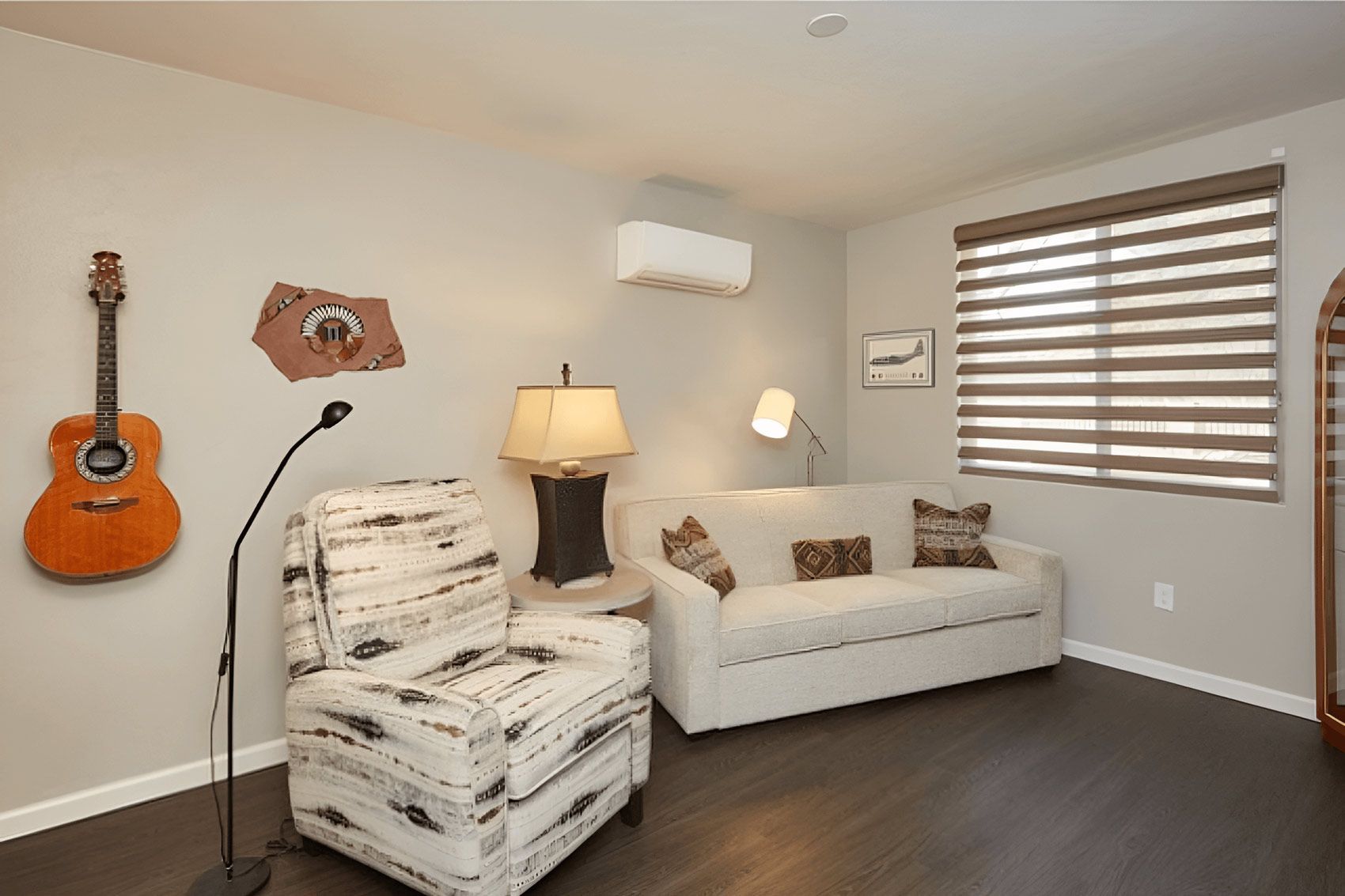A living room with a couch , chair , lamp and guitar on the wall.