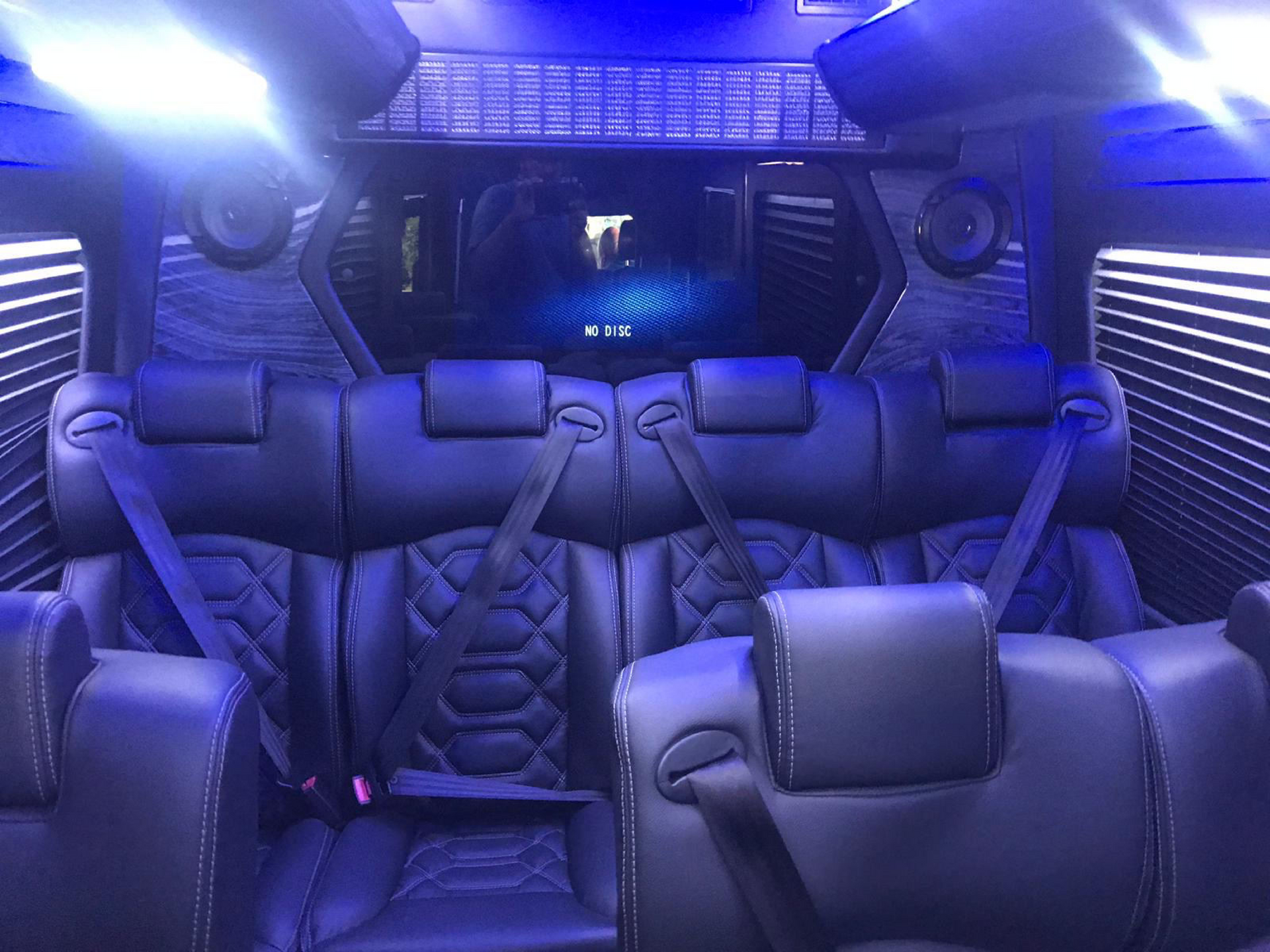 White Ford Transit van parked outside a store on a sunny day. A black pickup truck is in the background.