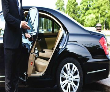 A person in a suit opens the door of a black car with tan interior.