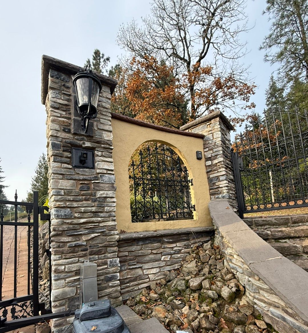 Person placing bricks along a stone wall, wearing gloves and a blue shirt; outdoor setting. Person placing bricks along a stone wall, wearing gloves and a blue shirt; outdoor setting.