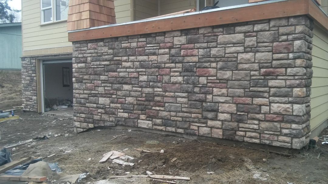 Stone wall with steps and a handrail leading up. Green grass and foliage in the background.