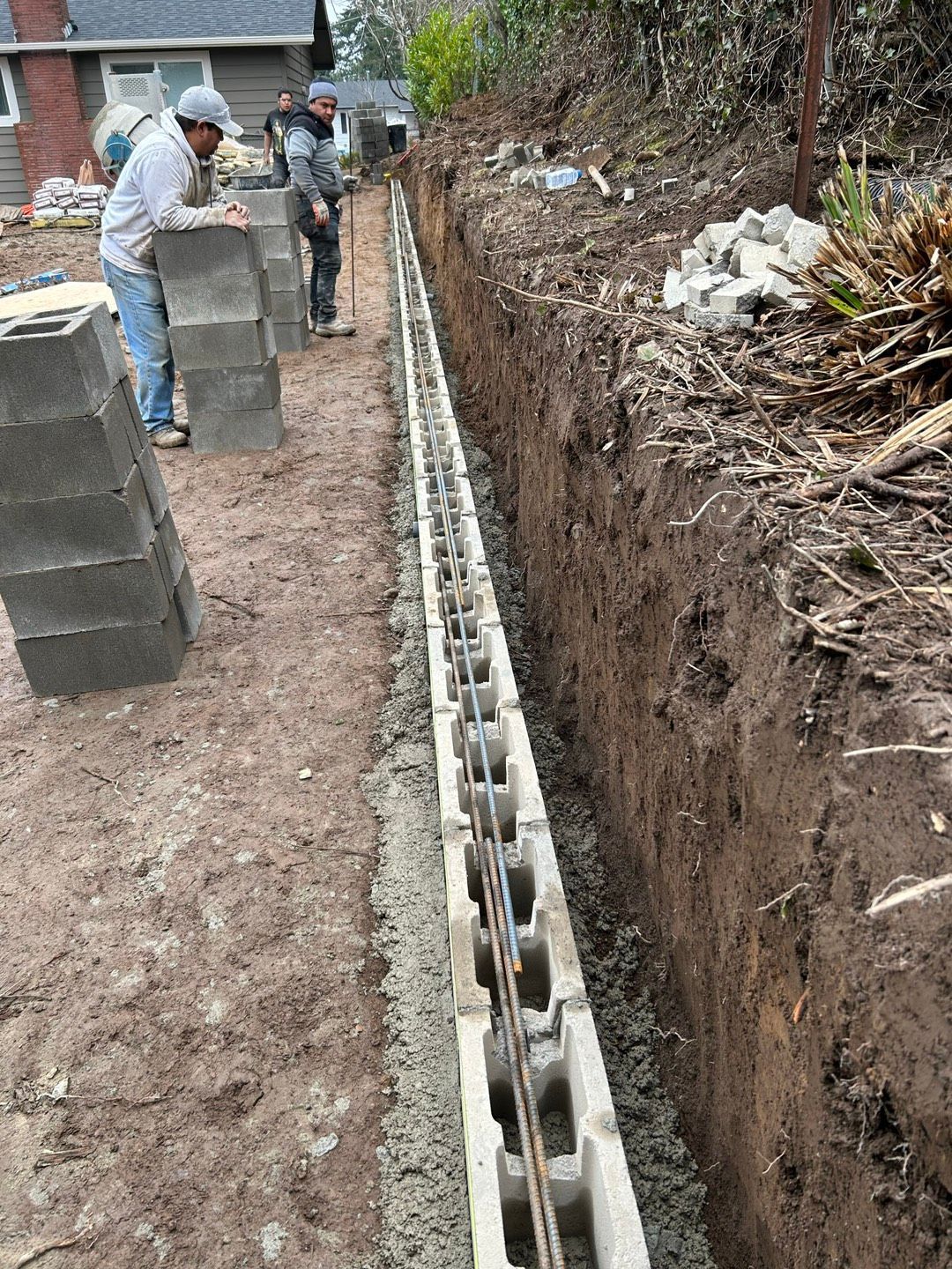 Construction worker with orange gloves, using a hammer on a concrete block wall.