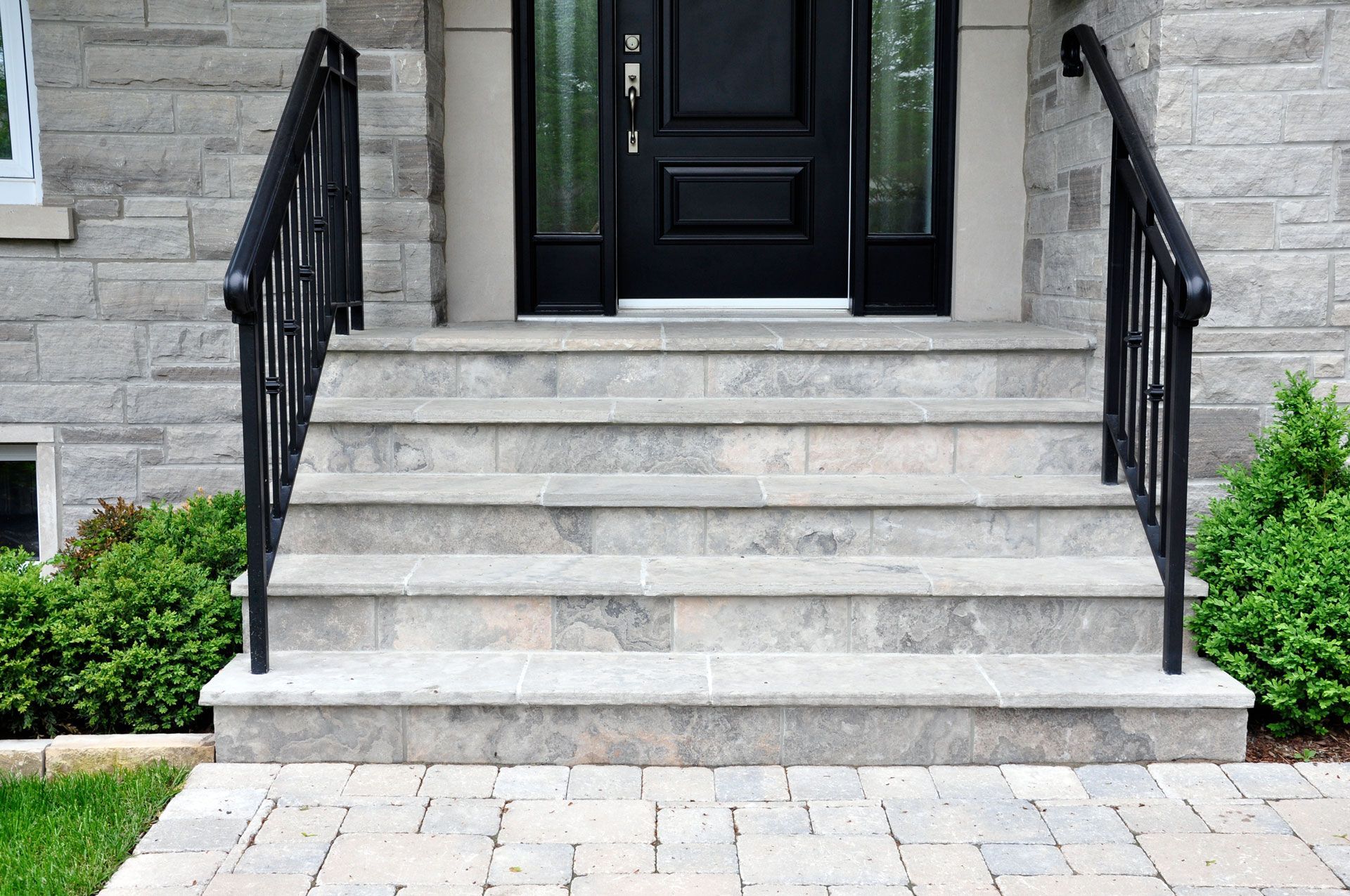 Stone steps leading to a black front door with sidelights, flanked by black railings and greenery. Stone steps leading to a black front door with sidelights, flanked by black railings and greenery.