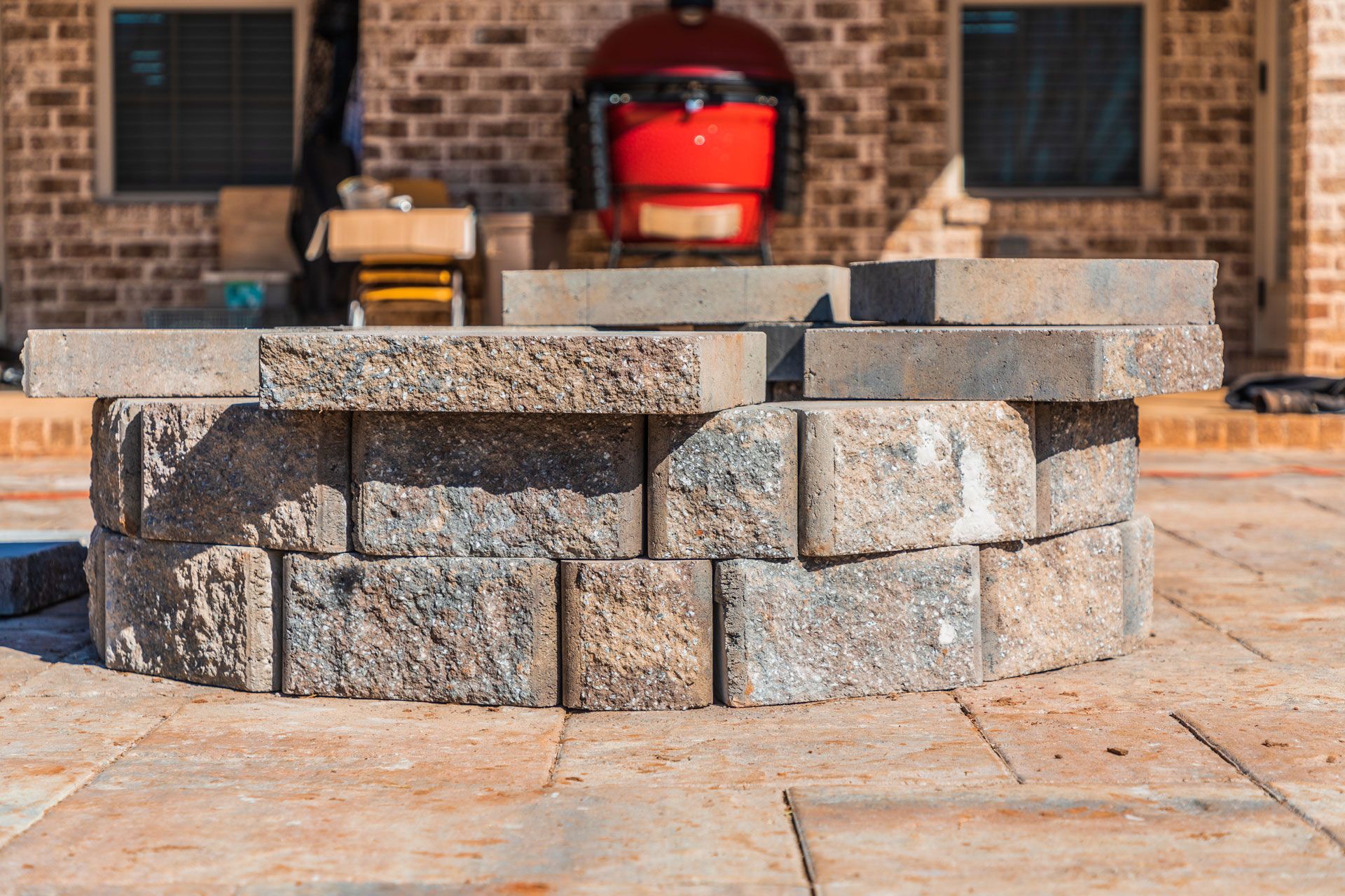 A partially constructed circular fire pit made of gray stone blocks on a stone patio.