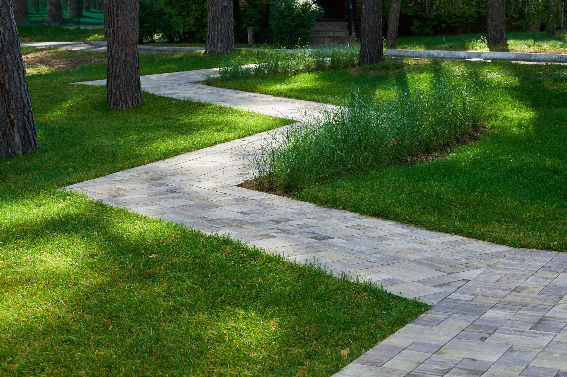 Stone pathway zigzags through green grass and trees in a sunny outdoor setting.