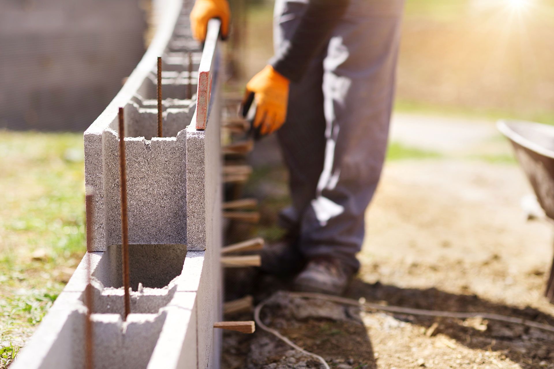 Construction worker building a concrete block wall, holding a block. Orange gloves, outdoor setting. Construction worker building a concrete block wall, holding a block. Orange gloves, outdoor setting.