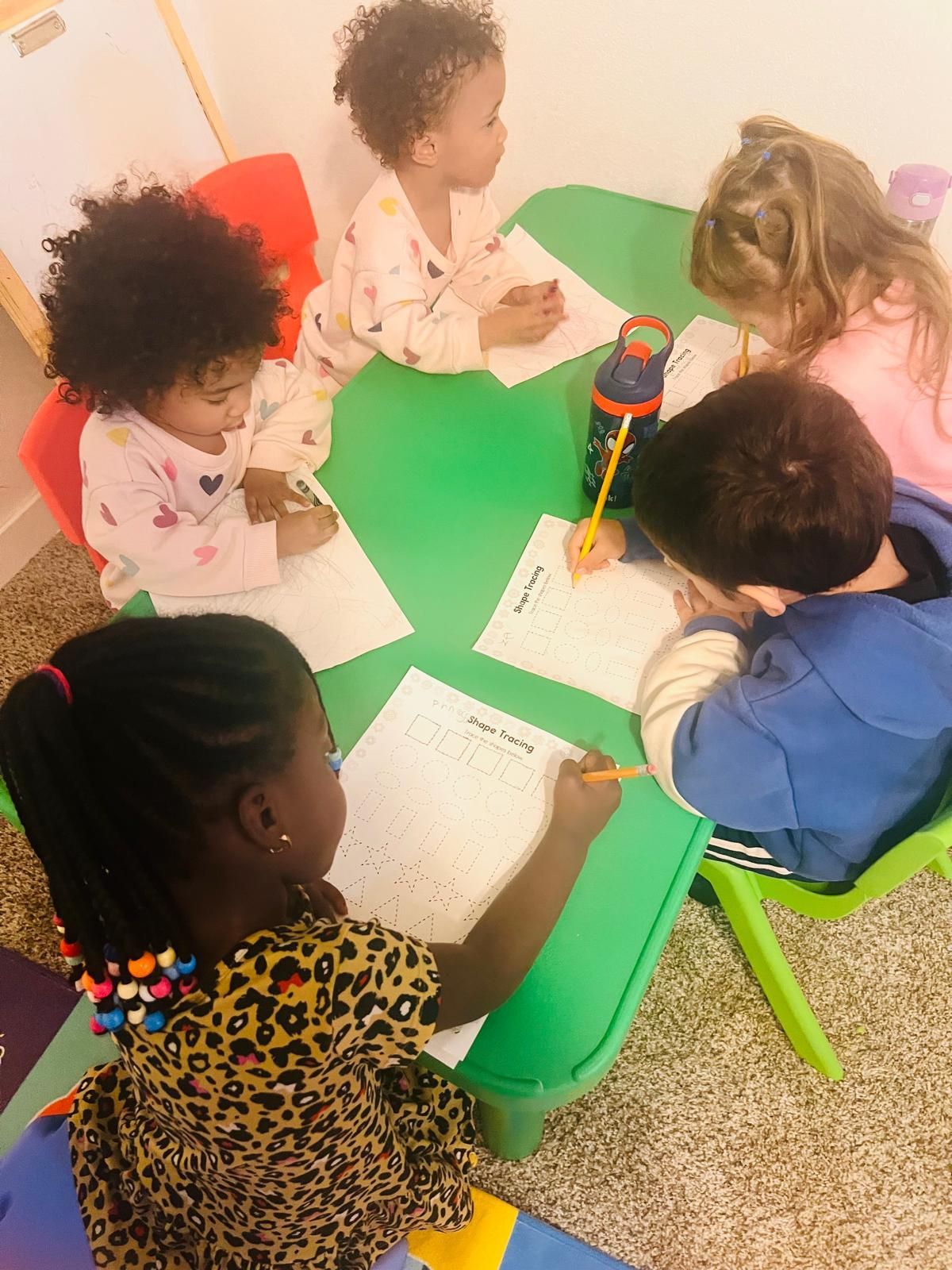 Children sitting at a green table, drawing on paper.
