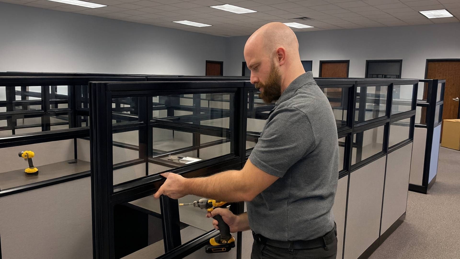 Man using a drill to assemble an office cubicle in an empty office.