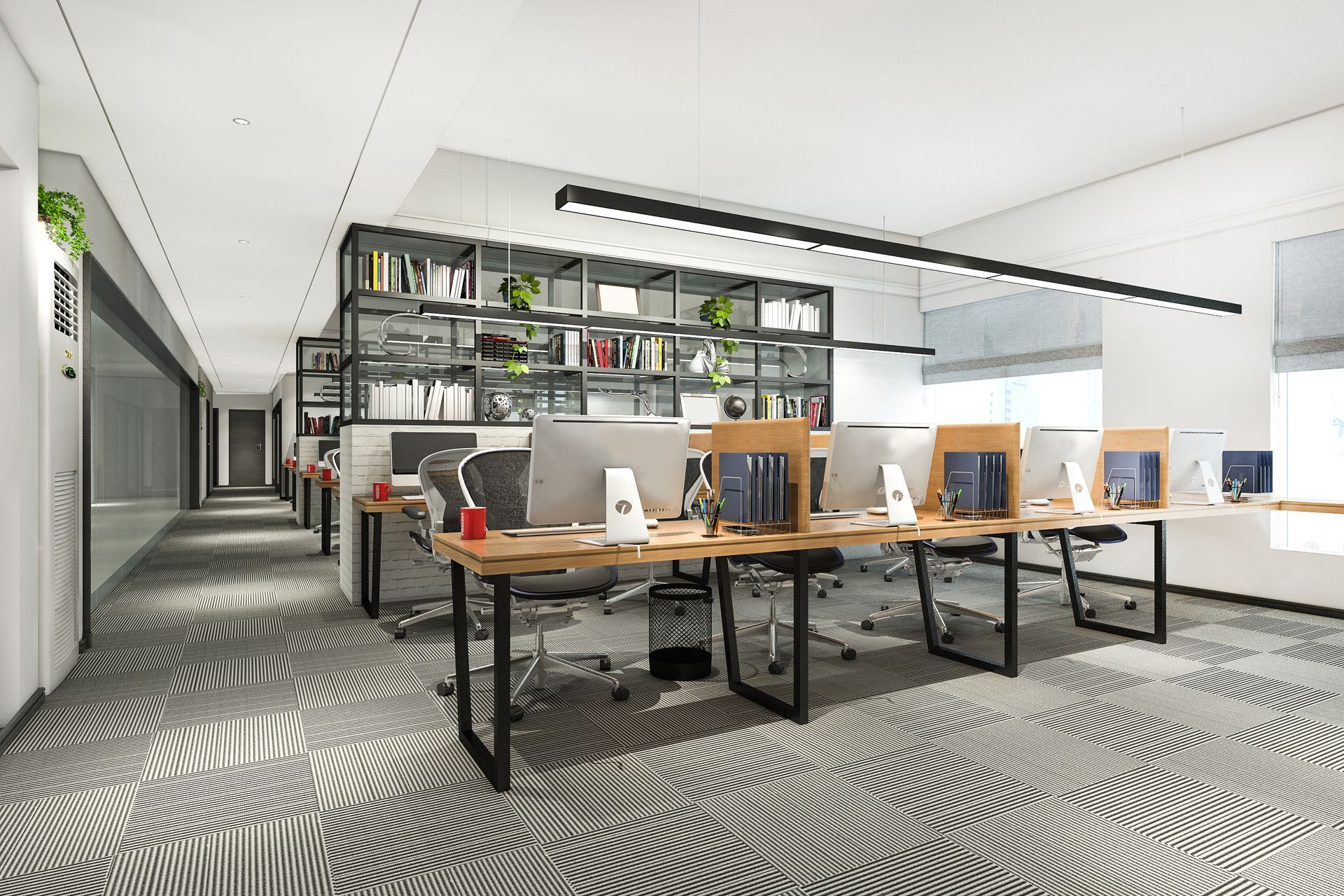 Modern open-plan office with desks, computers, and a large shelving unit on a patterned gray carpet.
