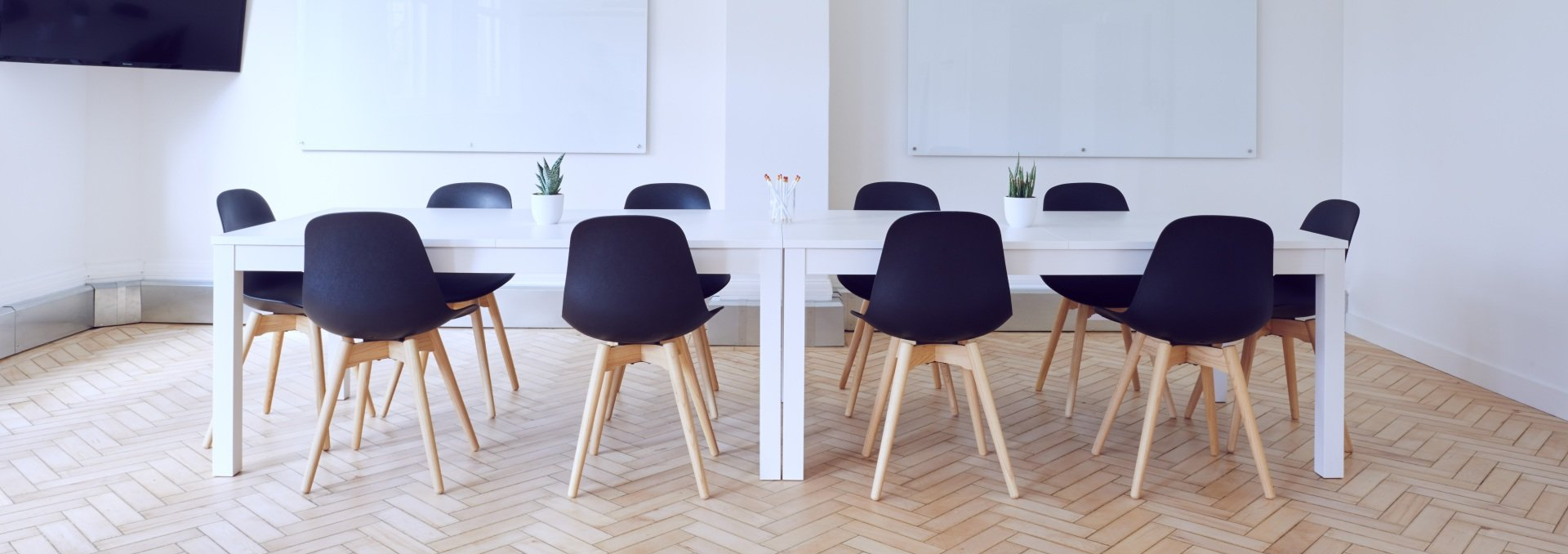Two white tables each with six black chairs are in a modern white room with whiteboards.
