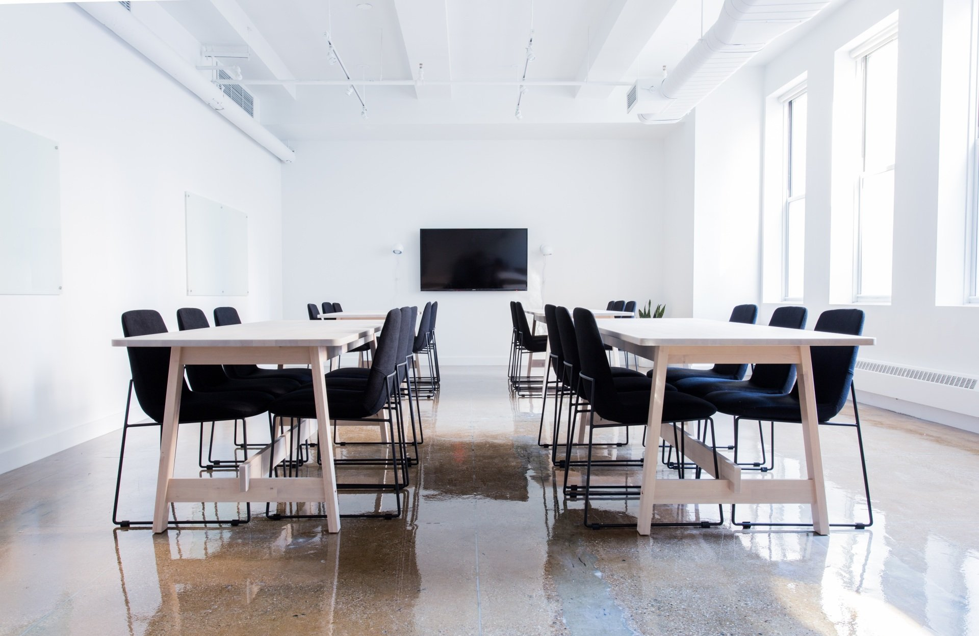 White classroom with tables, black chairs, and a large screen.