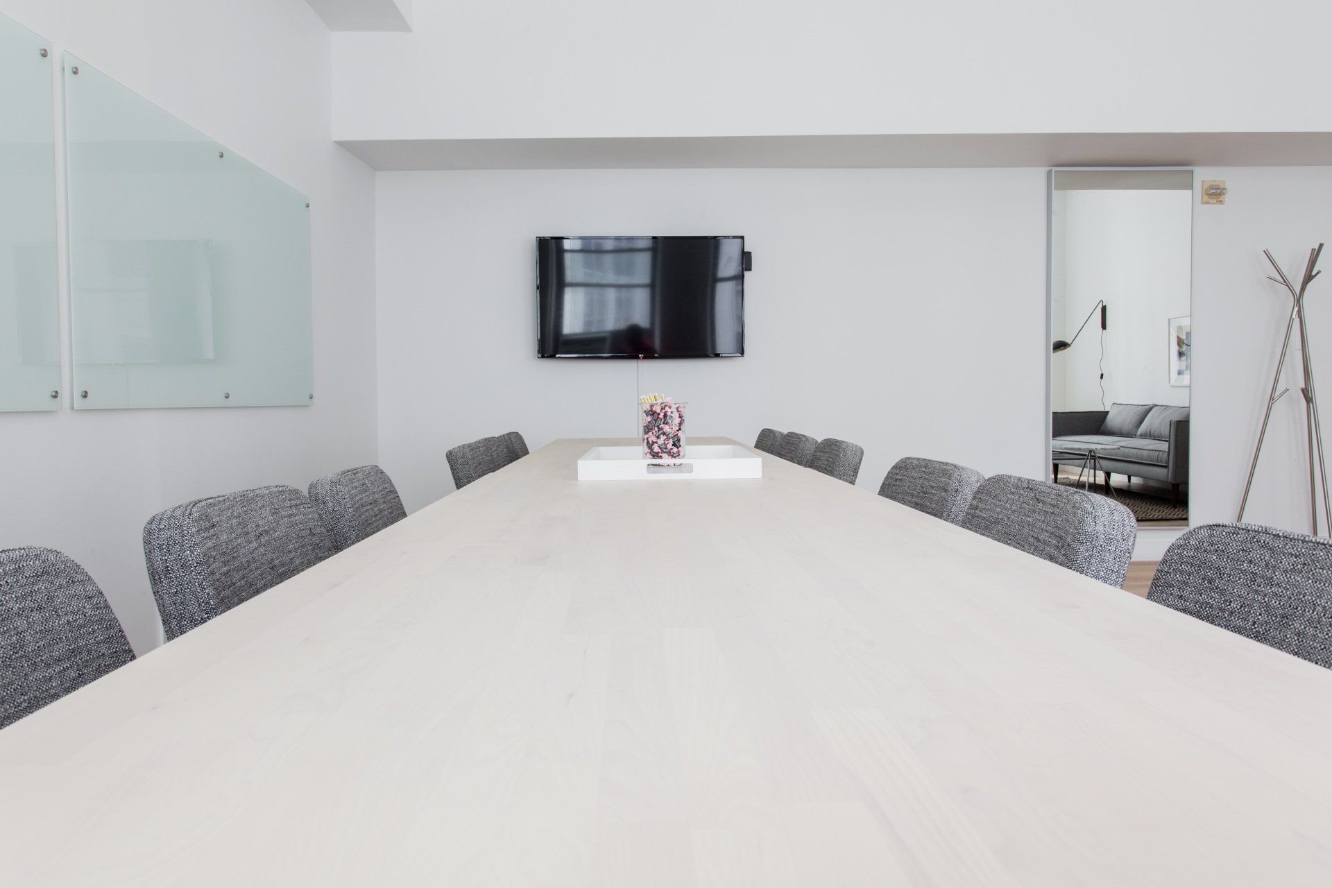 Conference room with long table, chairs, TV, and a whiteboard. White walls, modern design.