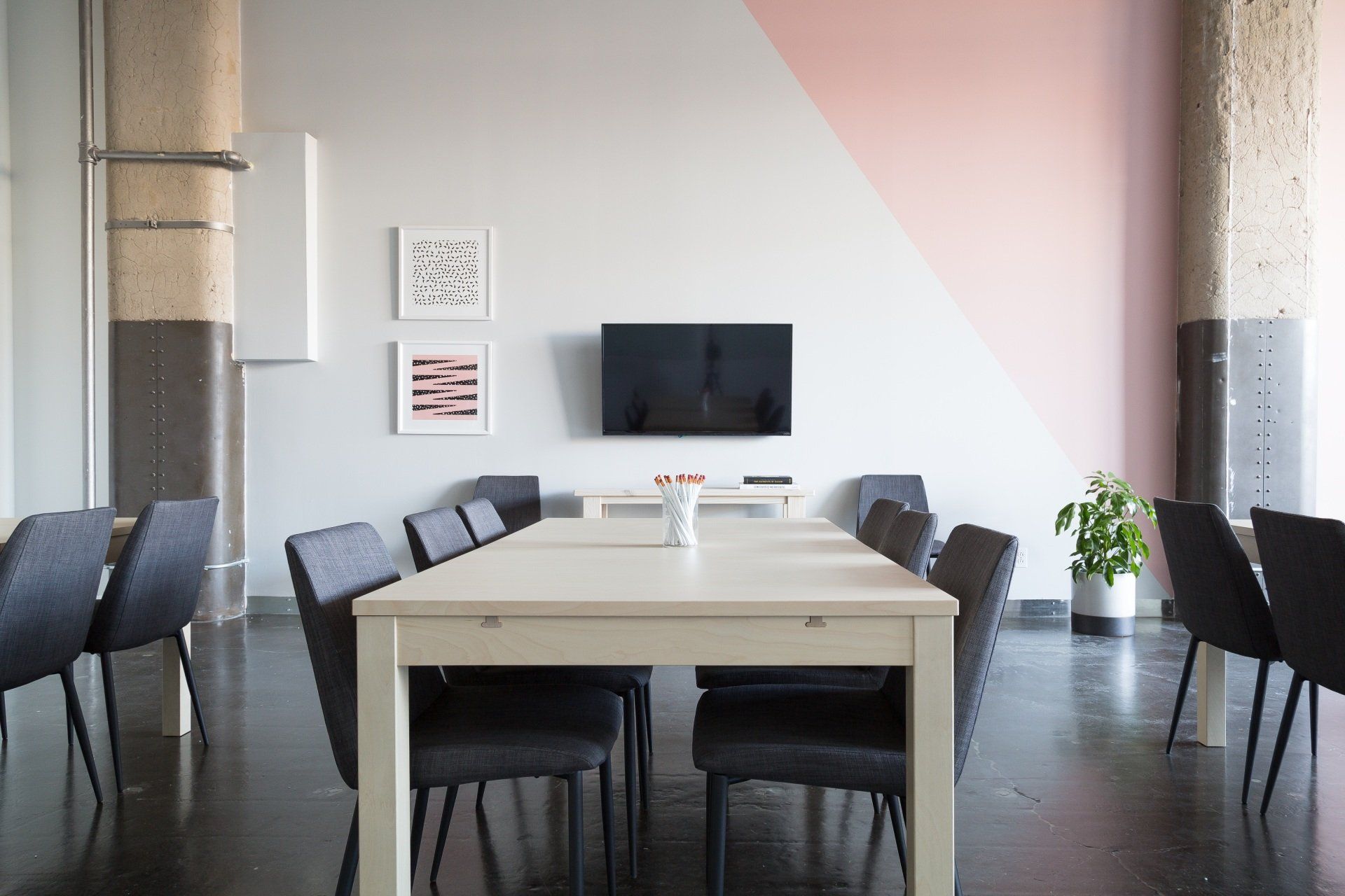 Meeting room with a long white table, black chairs, a TV, and a pink and gray painted wall.