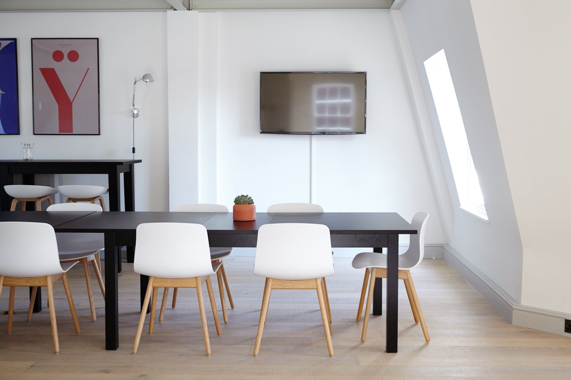 Modern meeting room with a dark table, white chairs, and a mounted TV.