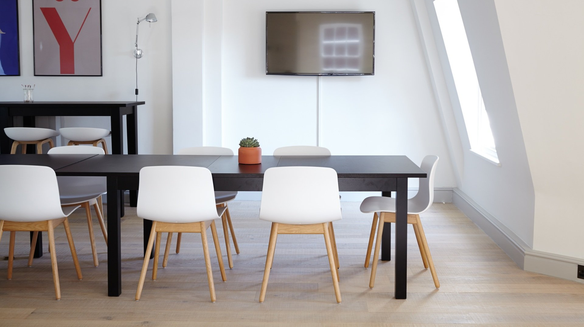 Modern dining area with a long black table, white chairs, and a TV on a white wall.