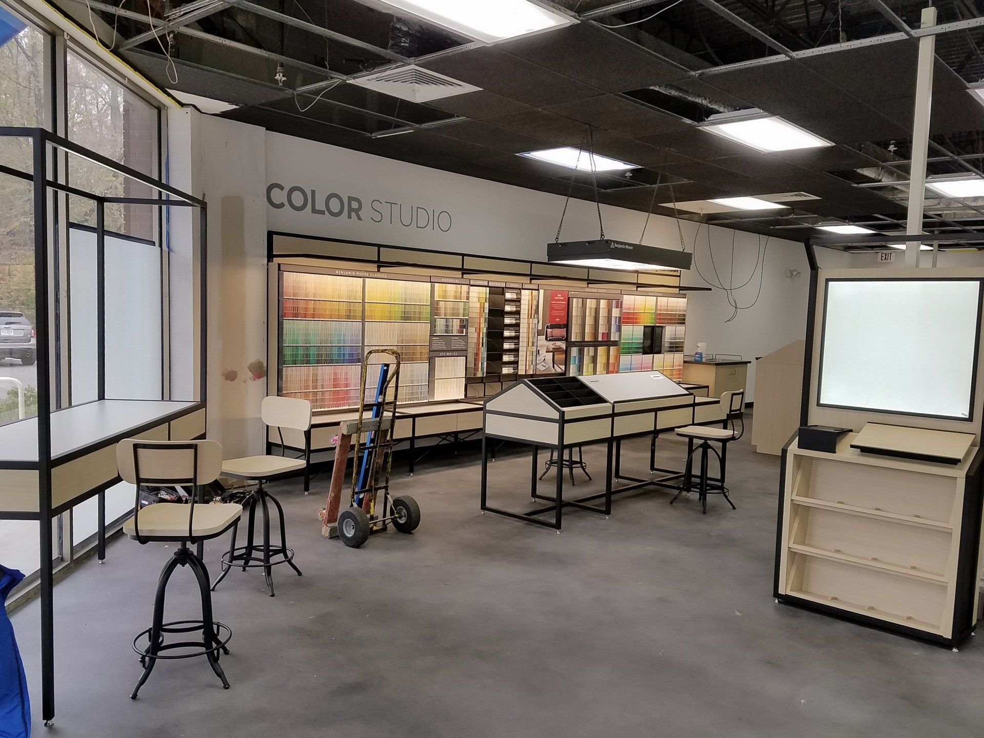Interior of a paint store with color swatches, displays, and tools on concrete floors, and stools.