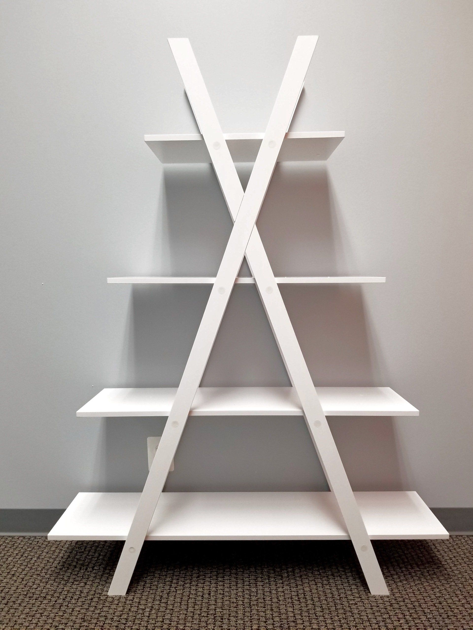 White, A-frame bookshelf with four shelves against a gray wall, sitting on a brown carpet.