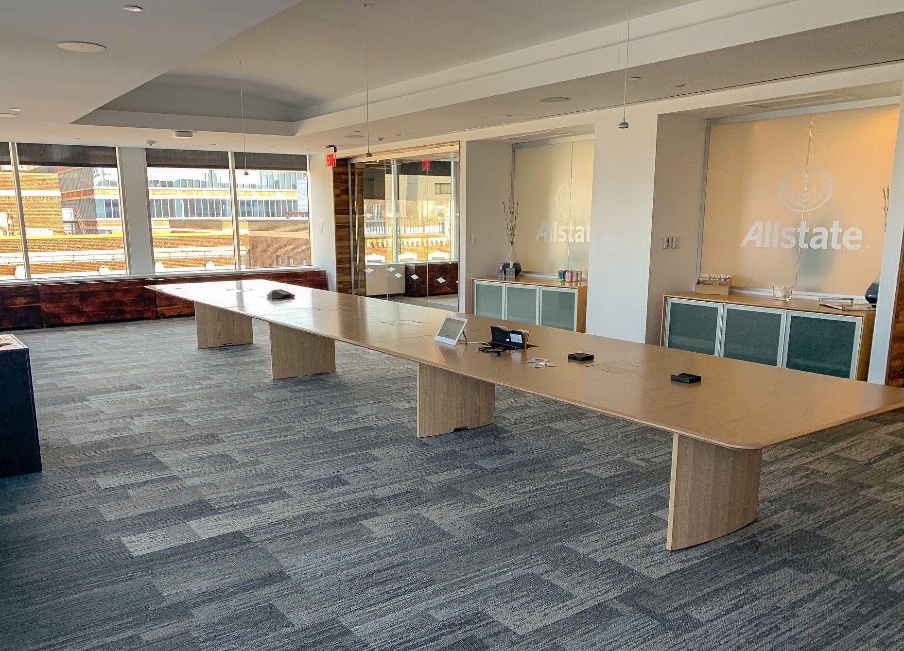 A long, light-wood conference table in a modern office space with the Allstate logo on the wall.