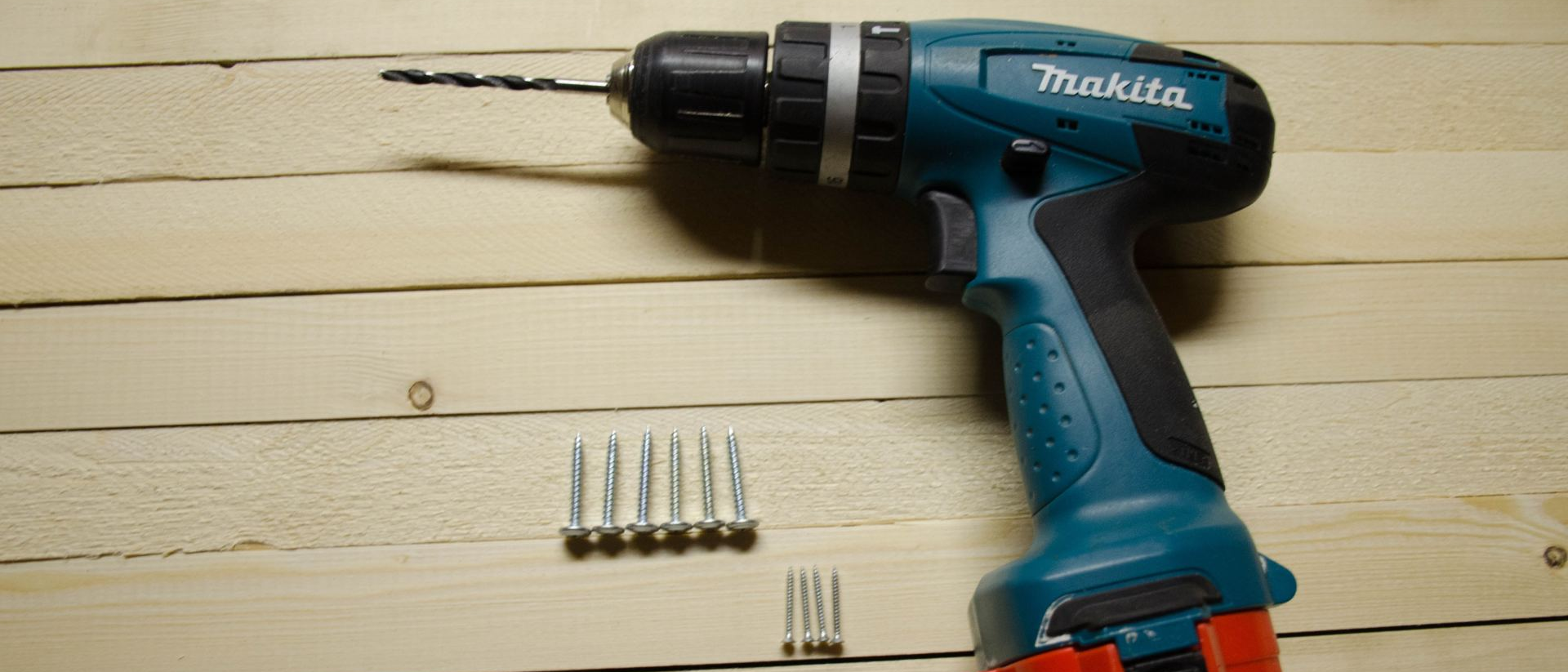 A Makita drill with a drill bit and several screws on a wooden surface.