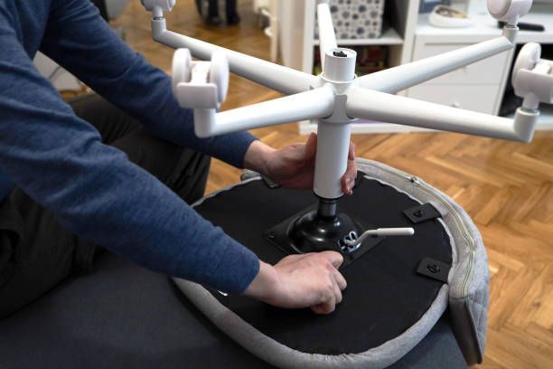 Person assembling a white office chair, attaching the base to the seat. Hands visible. Indoors.