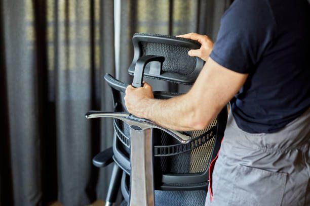 Person assembling an ergonomic office chair, hands on backrest, indoor setting.