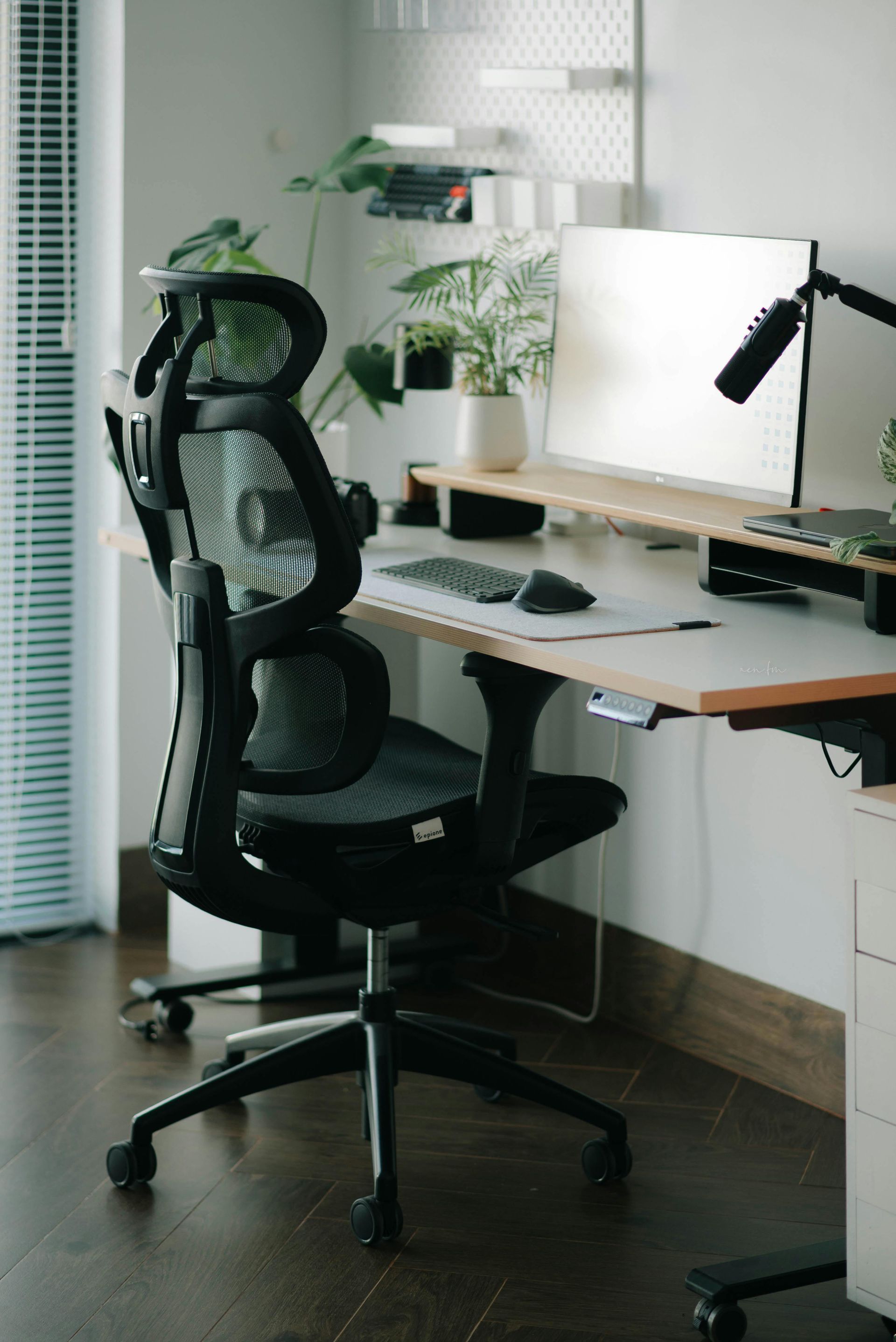 Ergonomic black office chair at a desk with a computer and microphone, indoor, natural light.