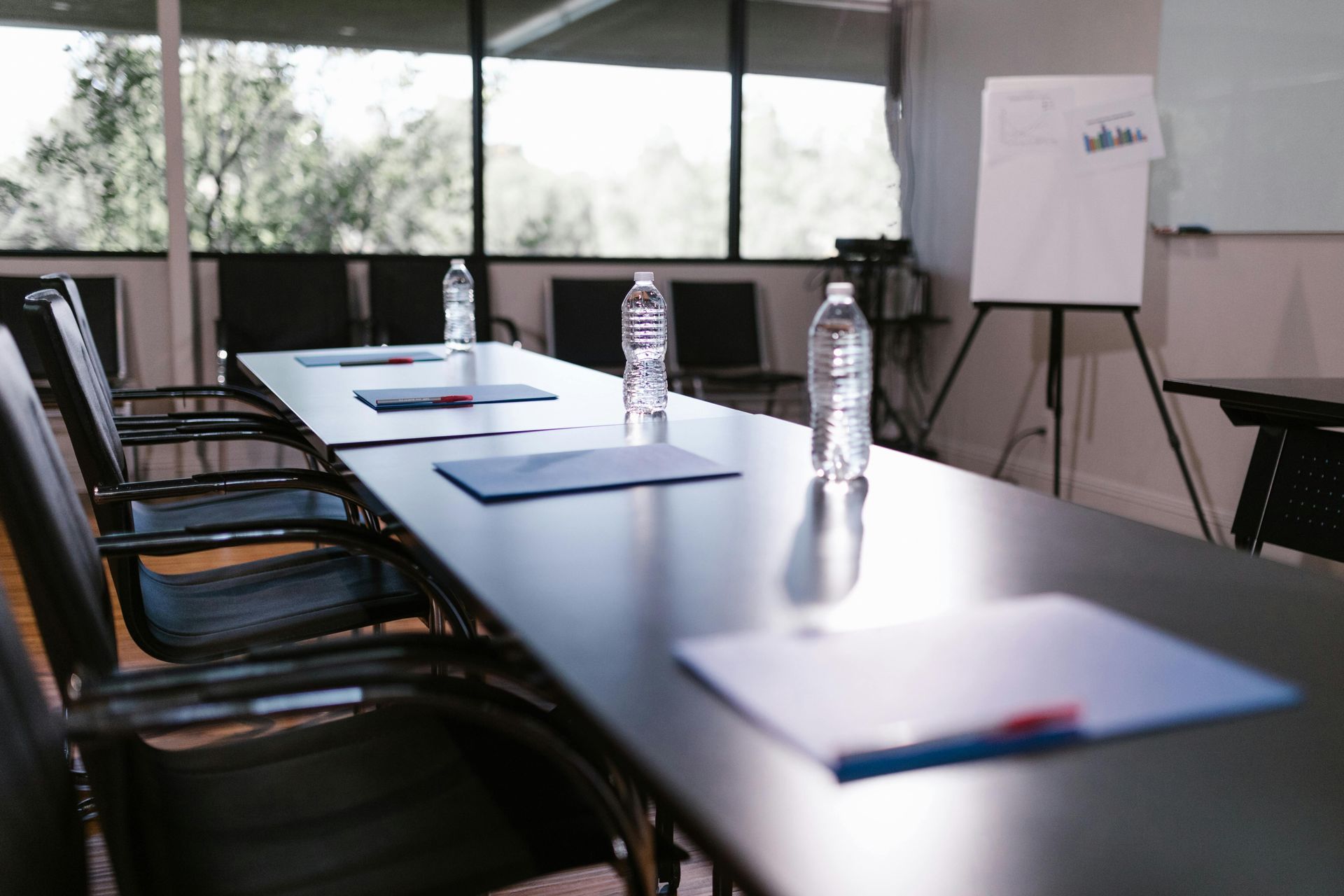 Conference room table with chairs, water bottles, and notebooks by a window and whiteboard