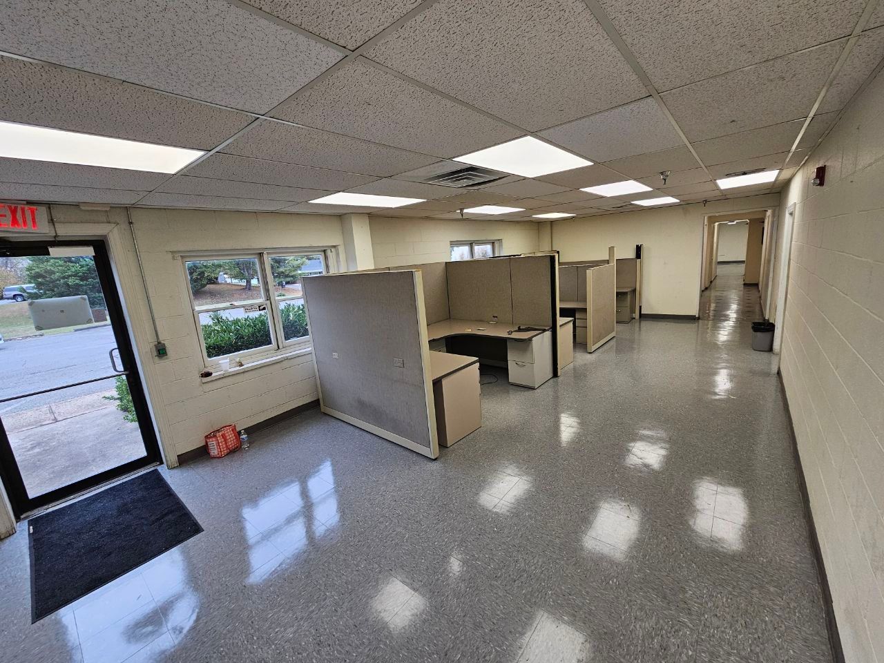 Empty office with cubicles, exit door, and reflective flooring.
