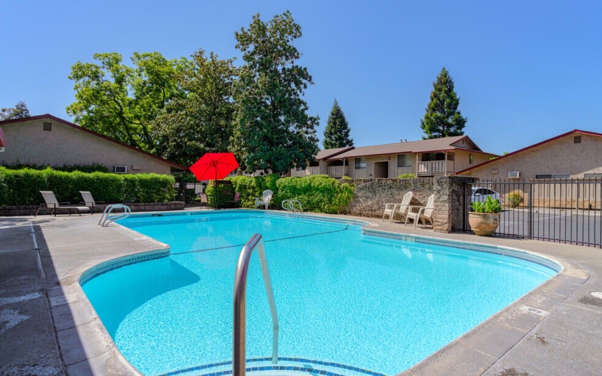 A large swimming pool with a red umbrella in the middle of it.