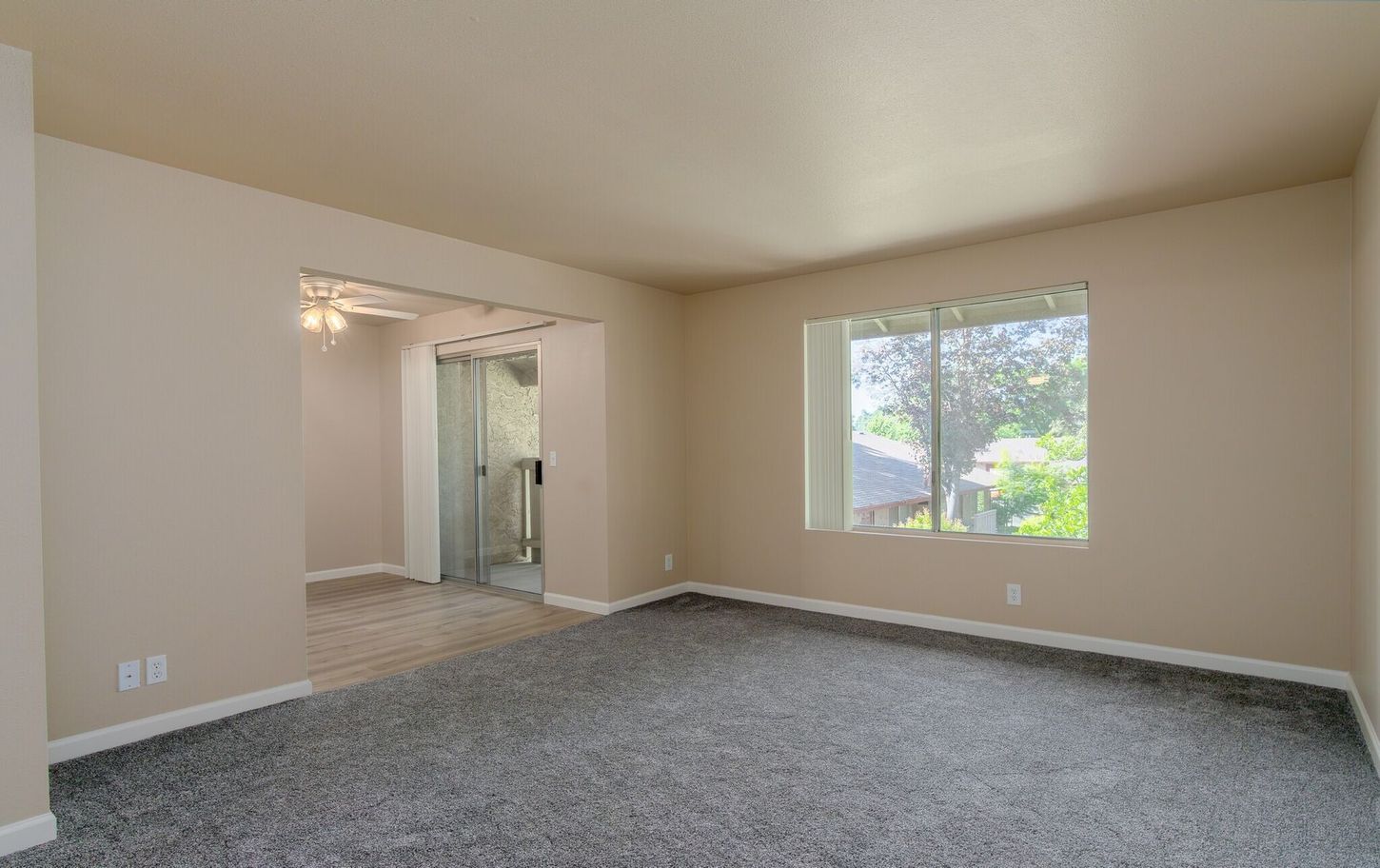 An empty living room with a large window and carpet.