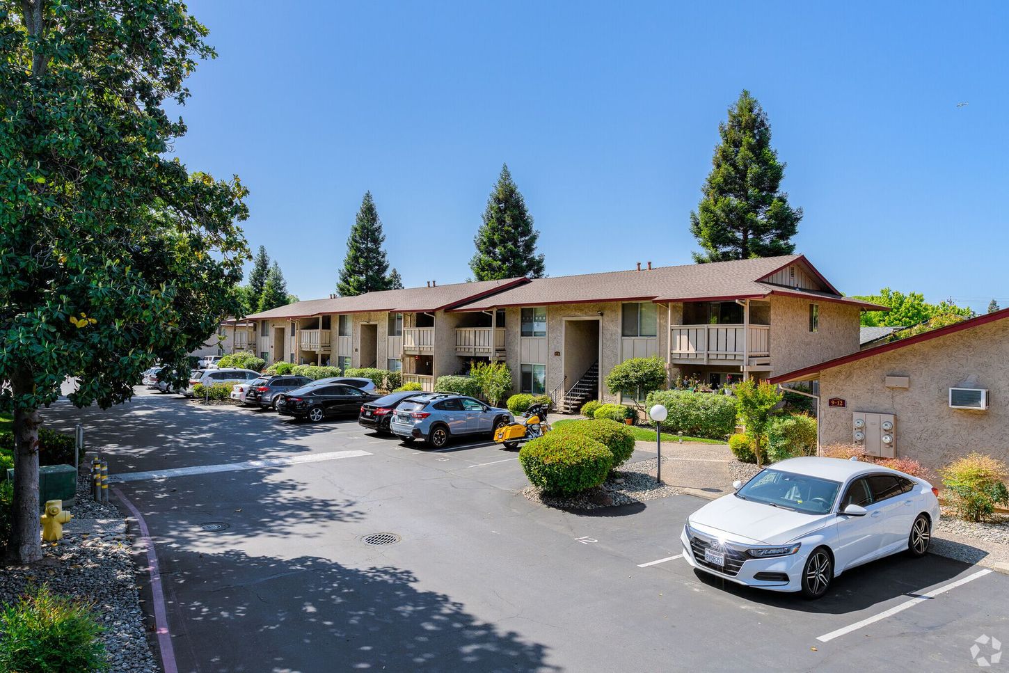 A white car is parked in front of a row of apartment buildings.