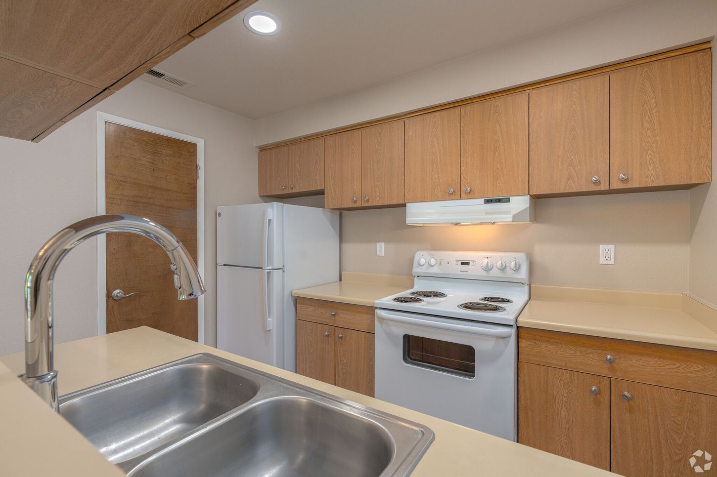 A kitchen with a sink , stove , refrigerator and cabinets.