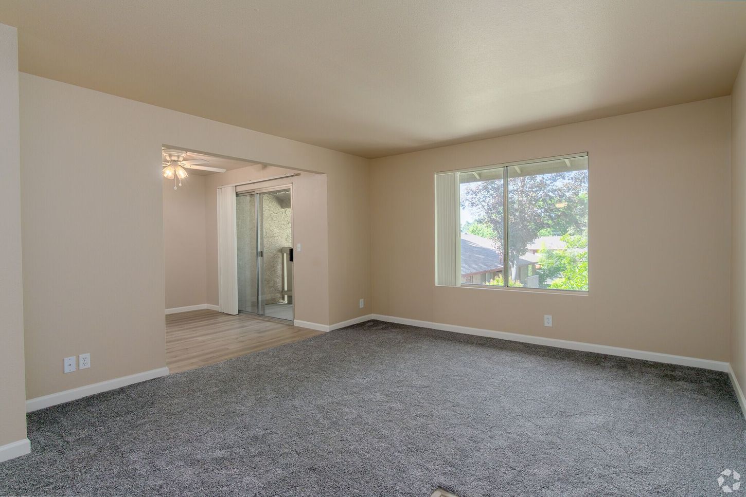 An empty living room with a carpeted floor and a window.
