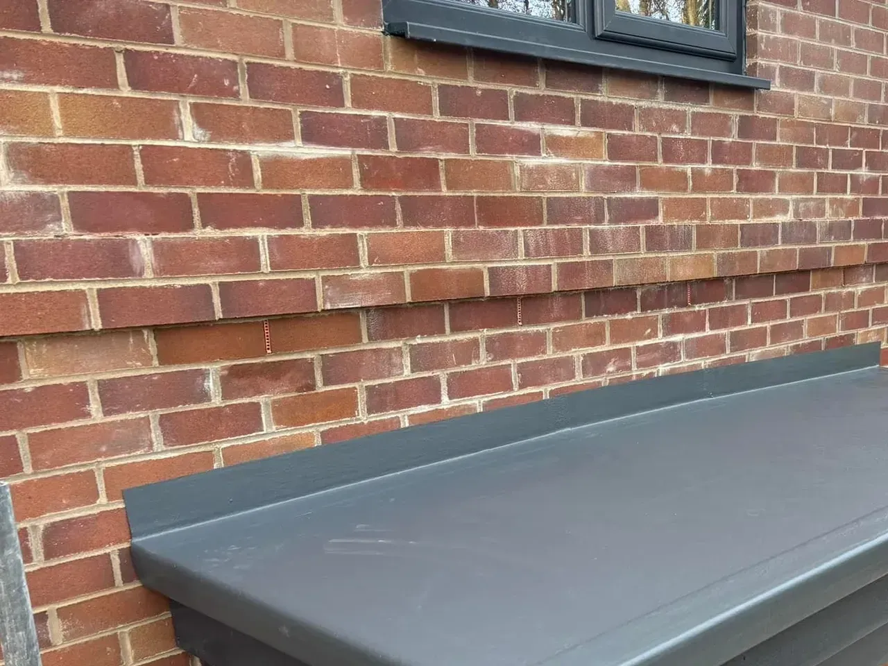 A brick wall with a window and a bench in front of it.