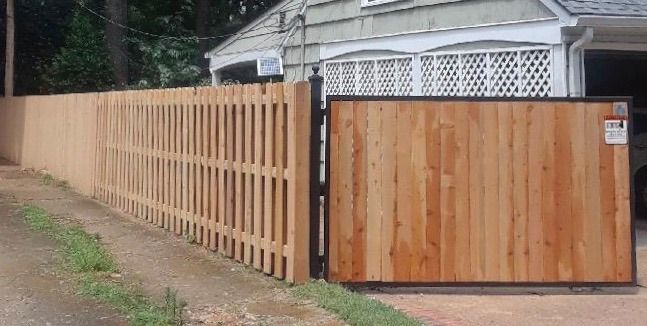 A wooden fence with a sliding gate in front of a house.