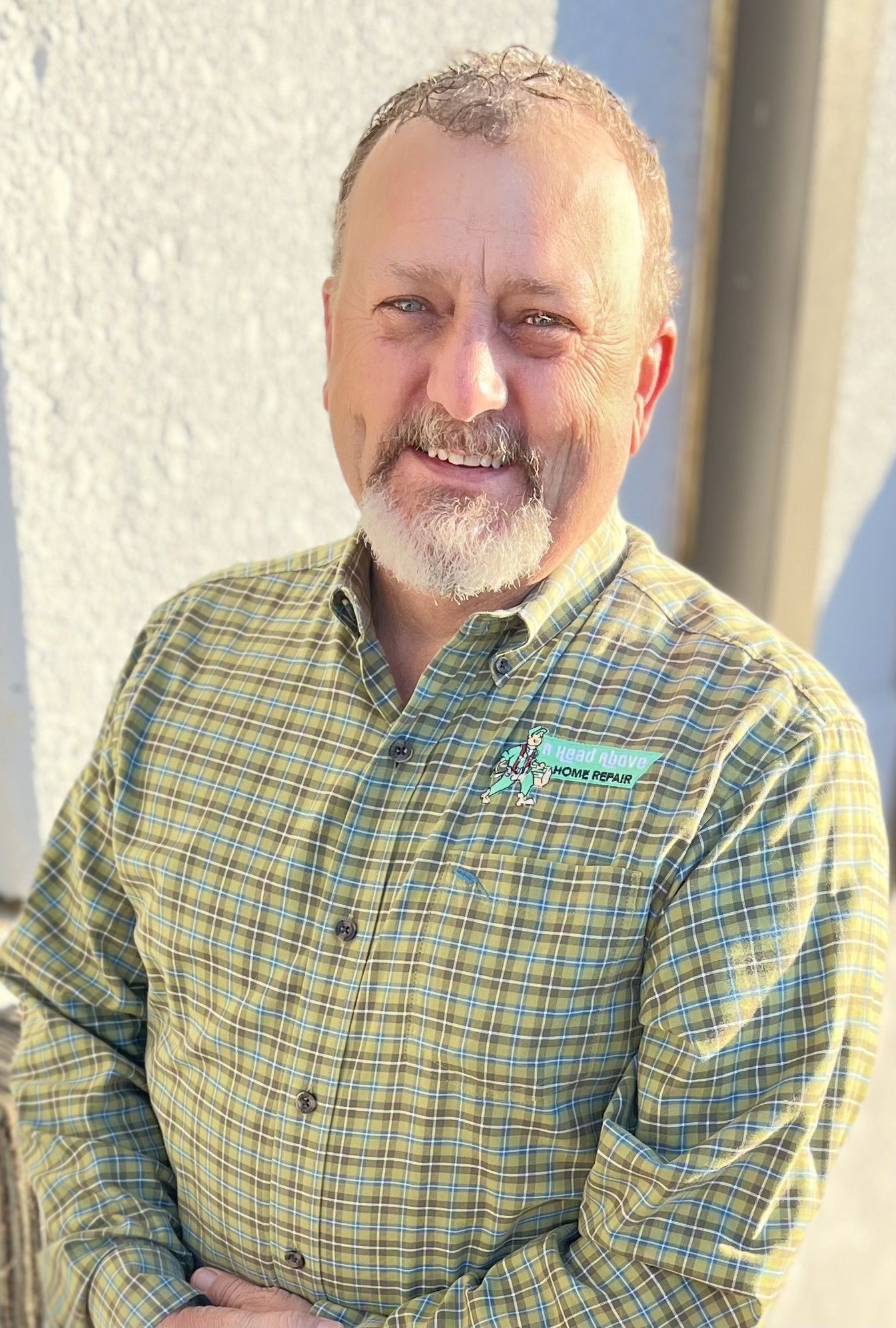 A man with a beard is wearing a plaid shirt and smiling for the camera.