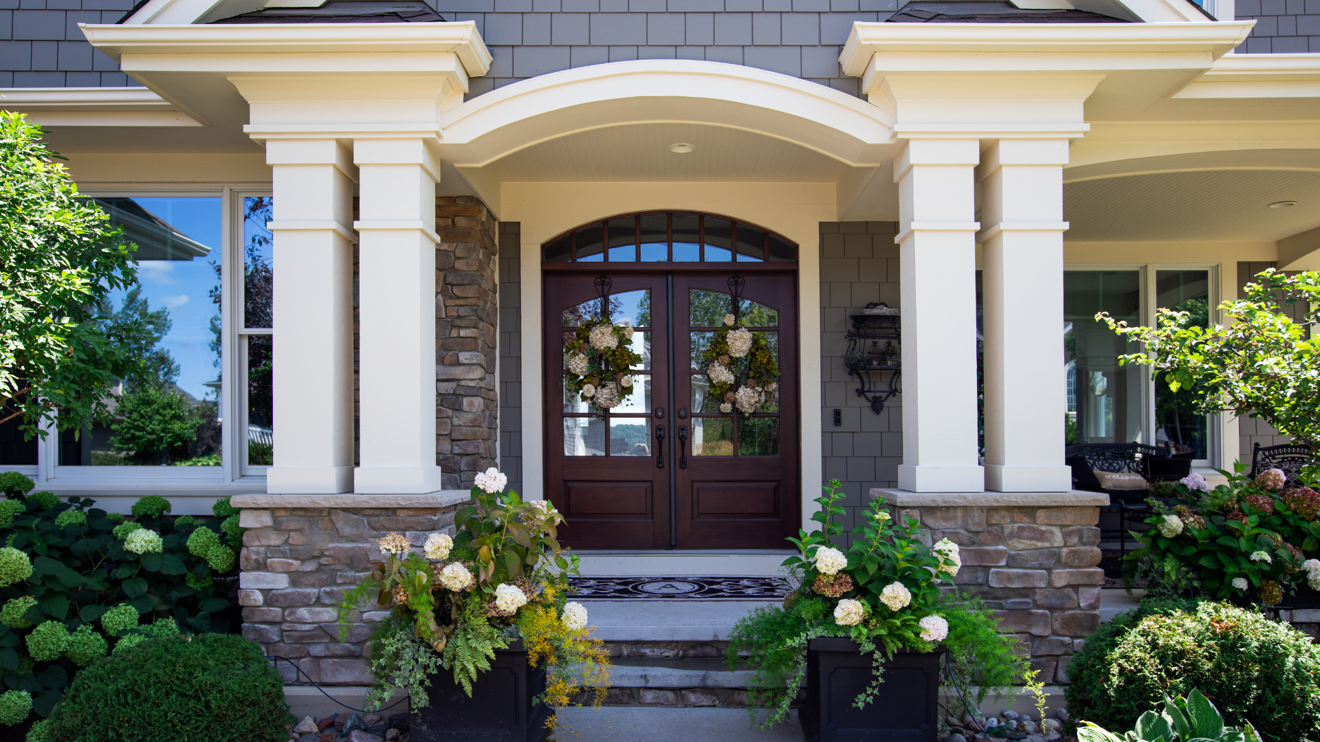 The front door of a house with a porch and flowers in front of it.