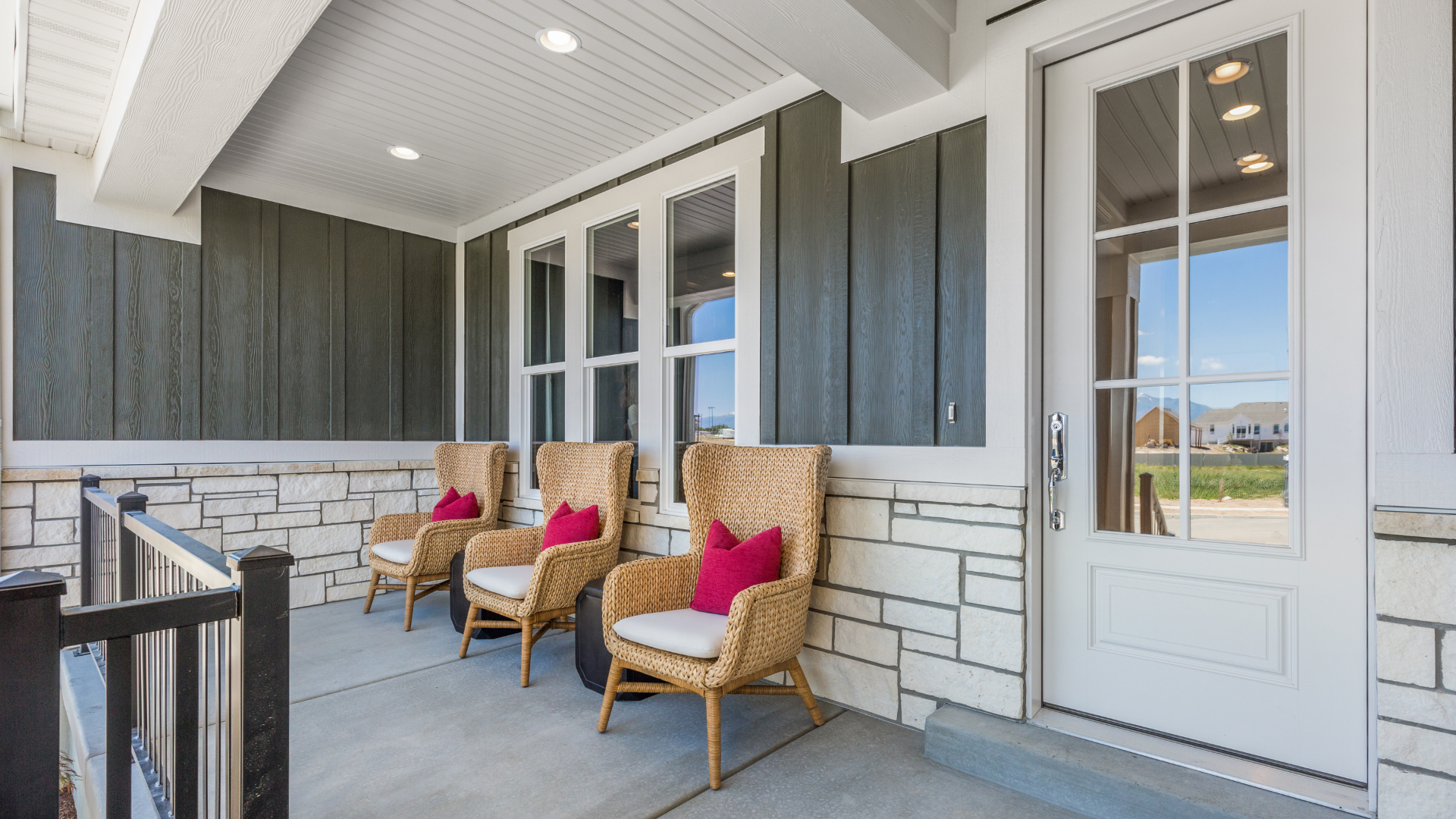 There are three chairs on the porch of a house.