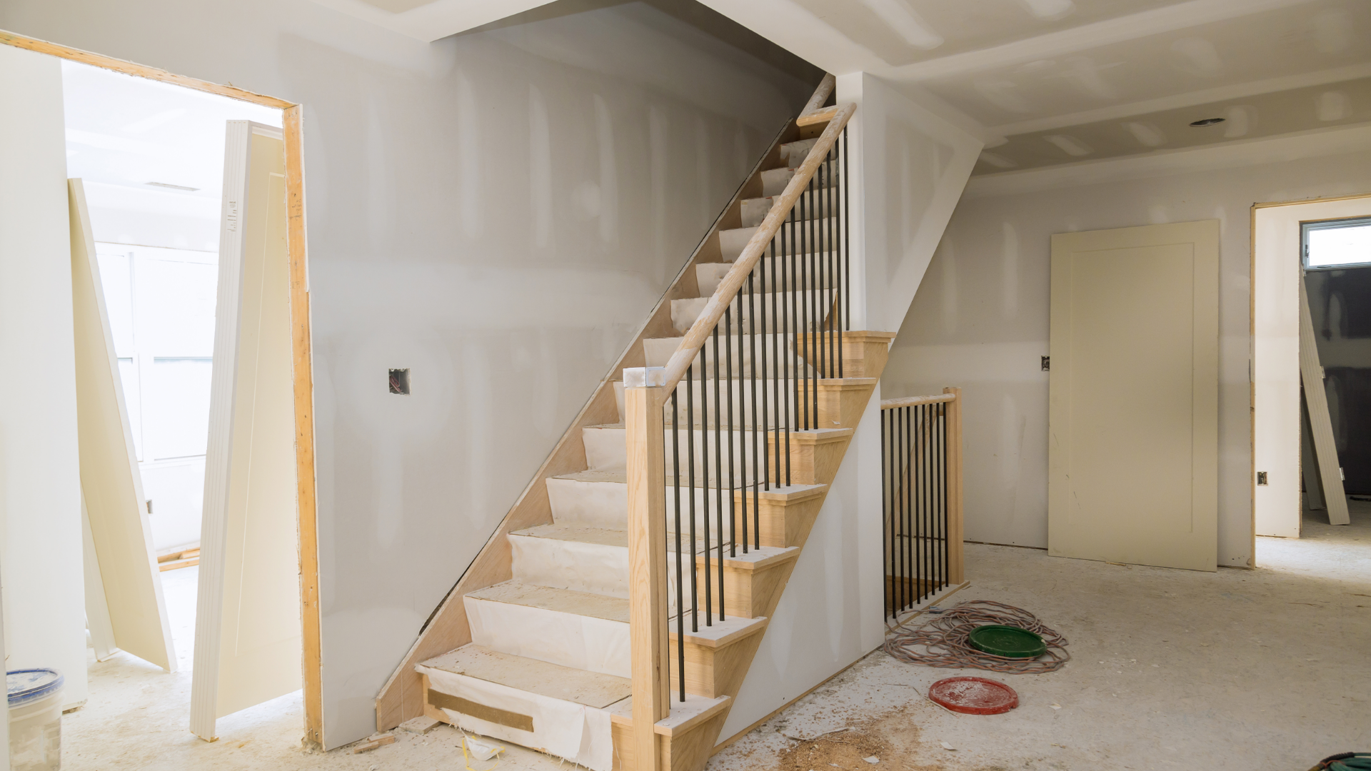 Interior view of a staircase during construction, featuring unfinished walls, wooden steps, and black metal railings.