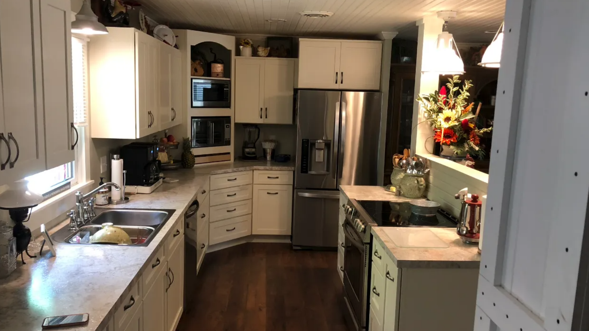 White kitchen with stainless steel appliances, countertops, and dark wood floors.