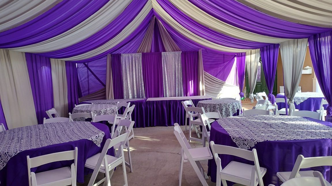 A tent with purple and white curtains and tables and chairs.