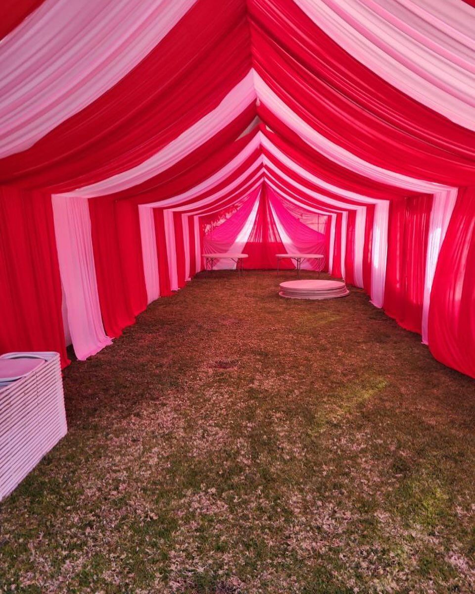 A red and white tent is sitting on top of a lush green field.