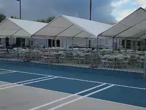 A row of white tents are sitting on top of a blue tennis court.