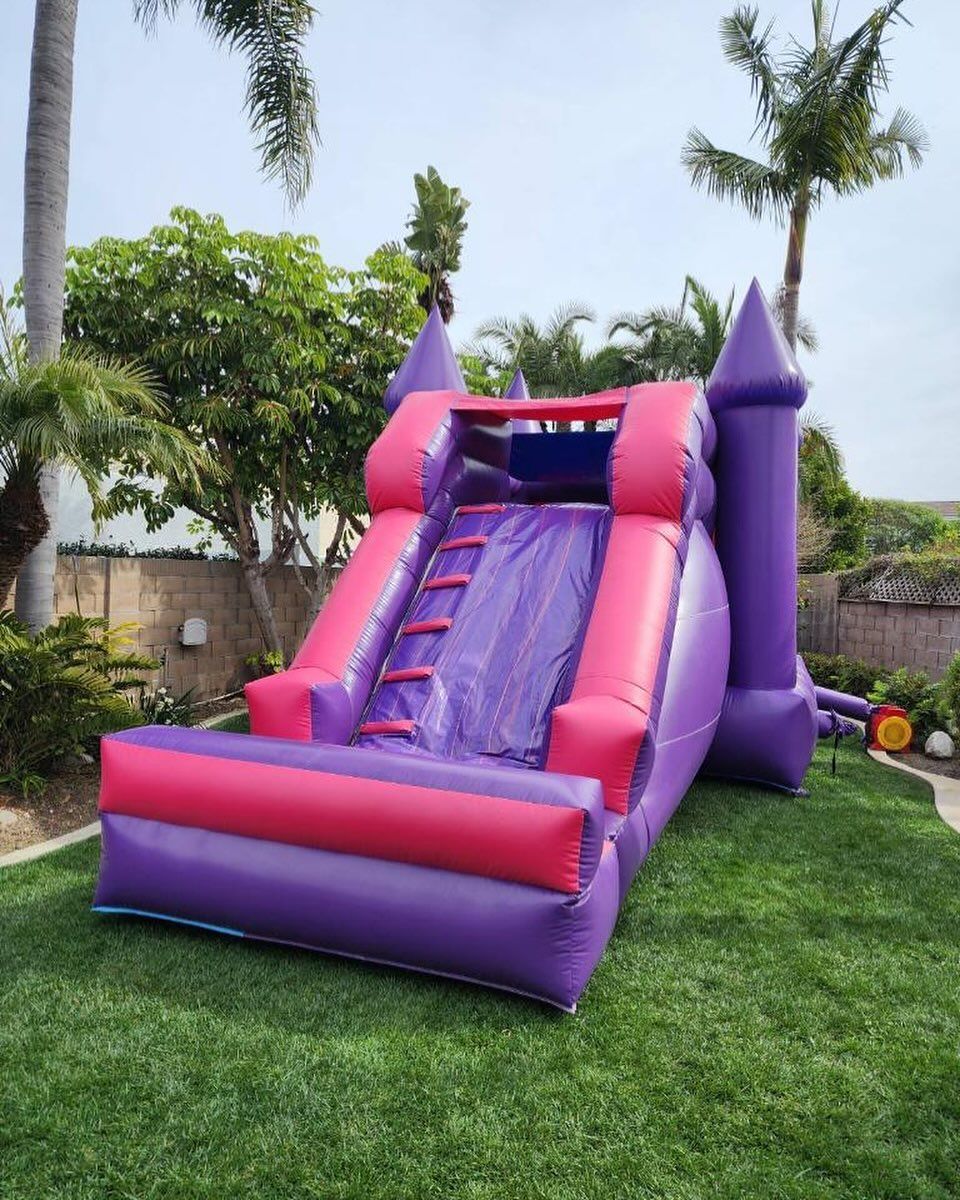 A purple and pink bouncy house is sitting on top of a lush green lawn.
