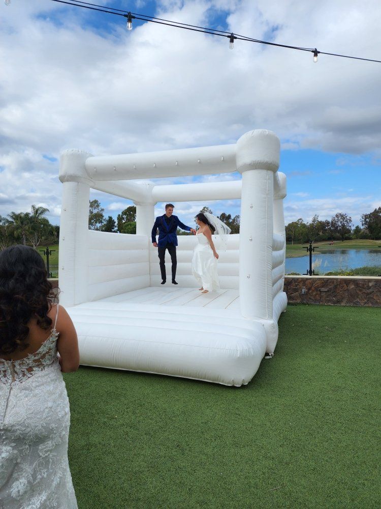 A bride and groom are standing in front of a white bouncy house.