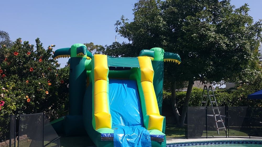 An inflatable crocodile water slide is sitting next to a swimming pool.