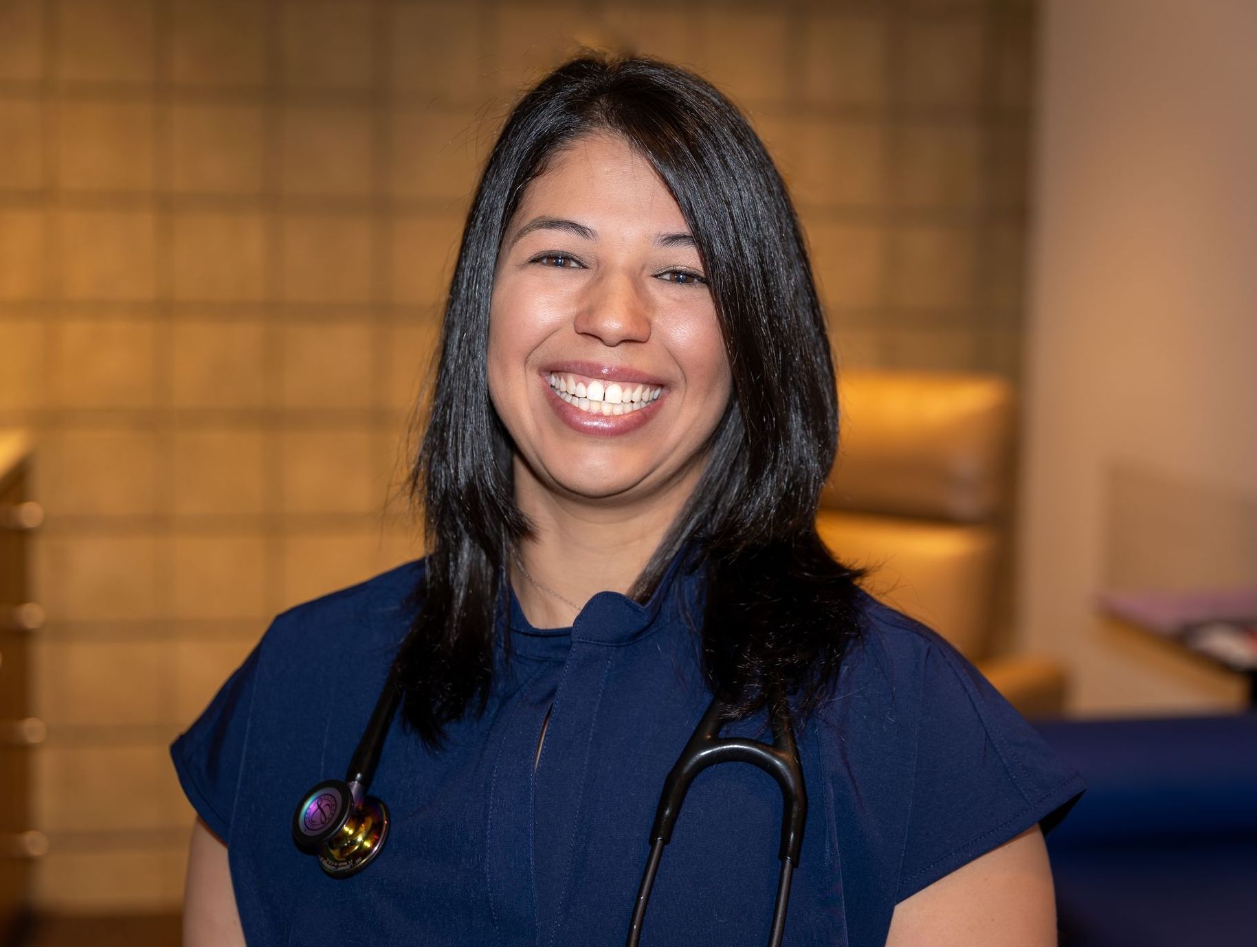 A woman with a stethoscope around her neck is smiling for the camera.